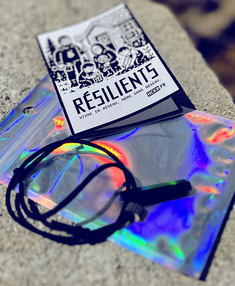 Le kit Résilients : livret fait main au slogan « vivre en réseau, même sans réseau », pochette holographique et bracelet brise-vitre en tungstène